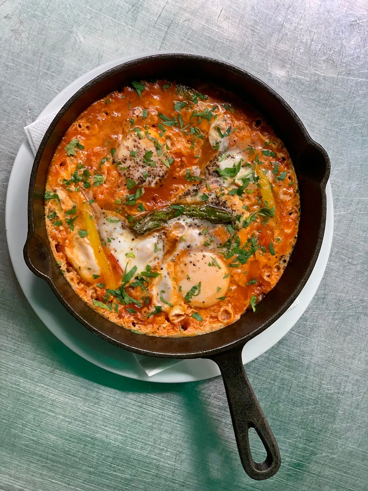 Top-down view of kosher shakshuka with poached eggs and herbs in a cast-iron skillet