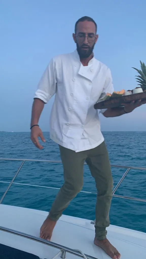 Chef Orel in chef's whites serving a fresh fruit platter aboard a yacht at dusk off Cancún