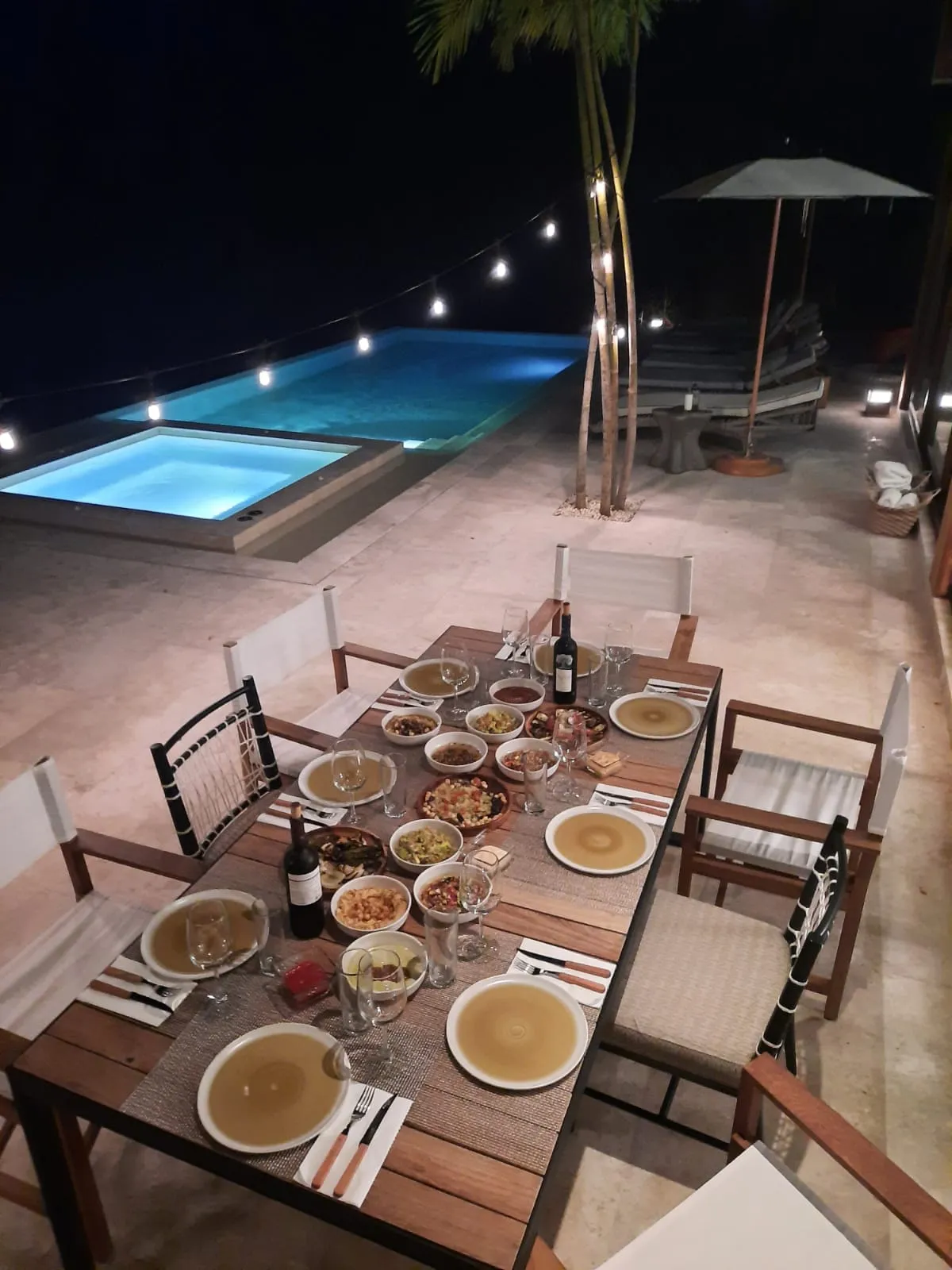 An elegant kosher dinner table set beside a lit infinity pool at night at a Riviera Maya villa